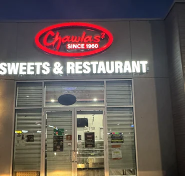 Chawlas² Sweets & Restaurant storefront at night with its lit red sign