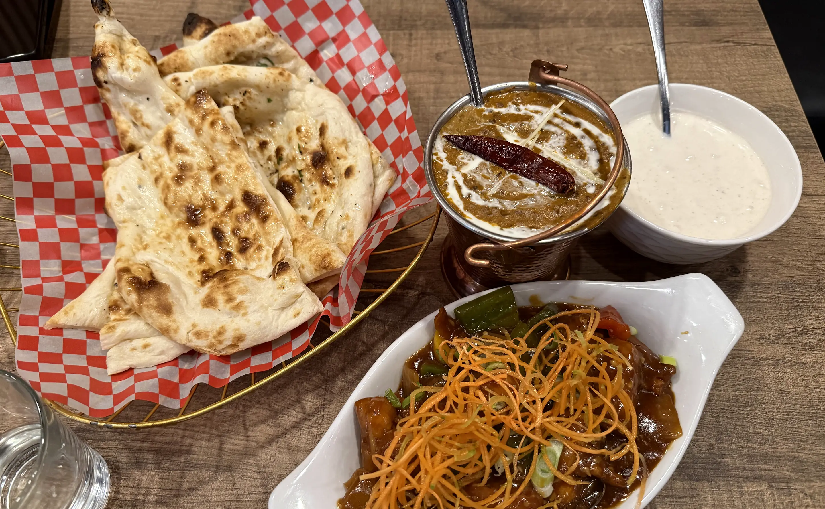 Butter naan basket with dal makhani, raita and a vegetable dish on a wooden table