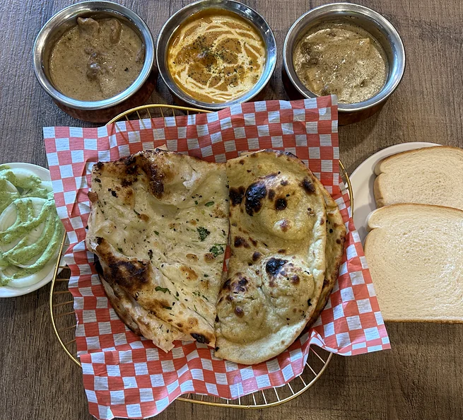Butter naan in a checkered basket with three curries, white bread and mint chutney