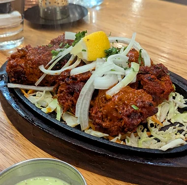 Red-marinated chicken pieces on a sizzler with onion, lemon and cabbage, with mint chutney