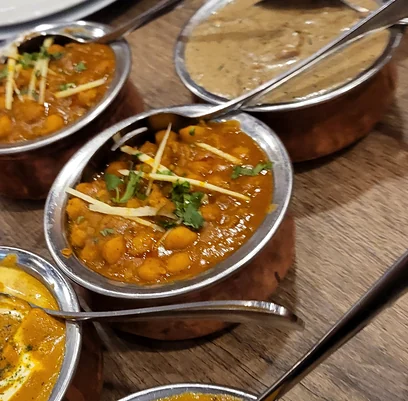 Chickpea curry with ginger garnish and creamy curries in steel bowls