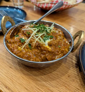 Curry garnished with ginger and coriander in a steel karahi