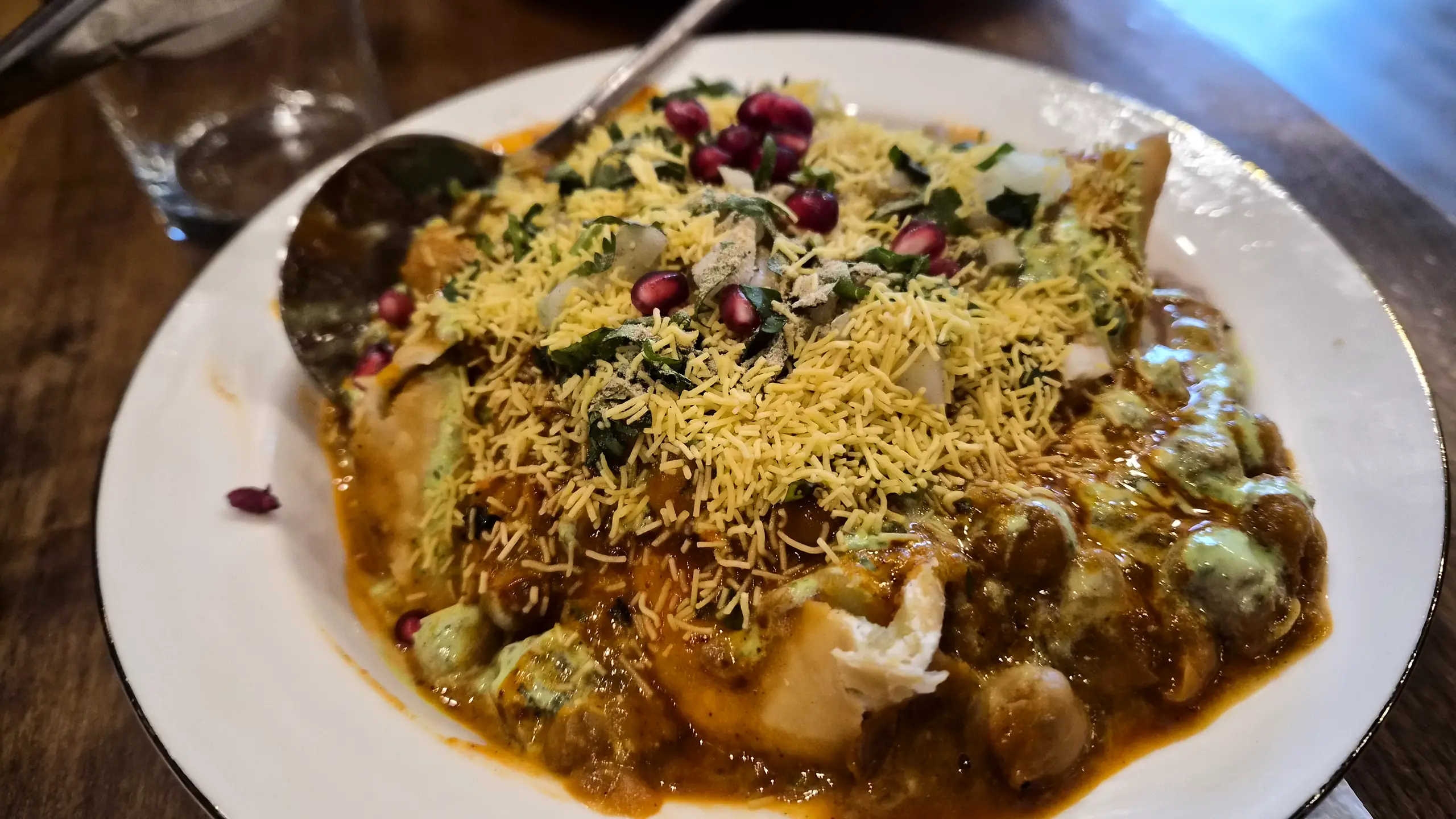 Chaat topped with sev, pomegranate seeds, chickpeas and coriander on a white plate