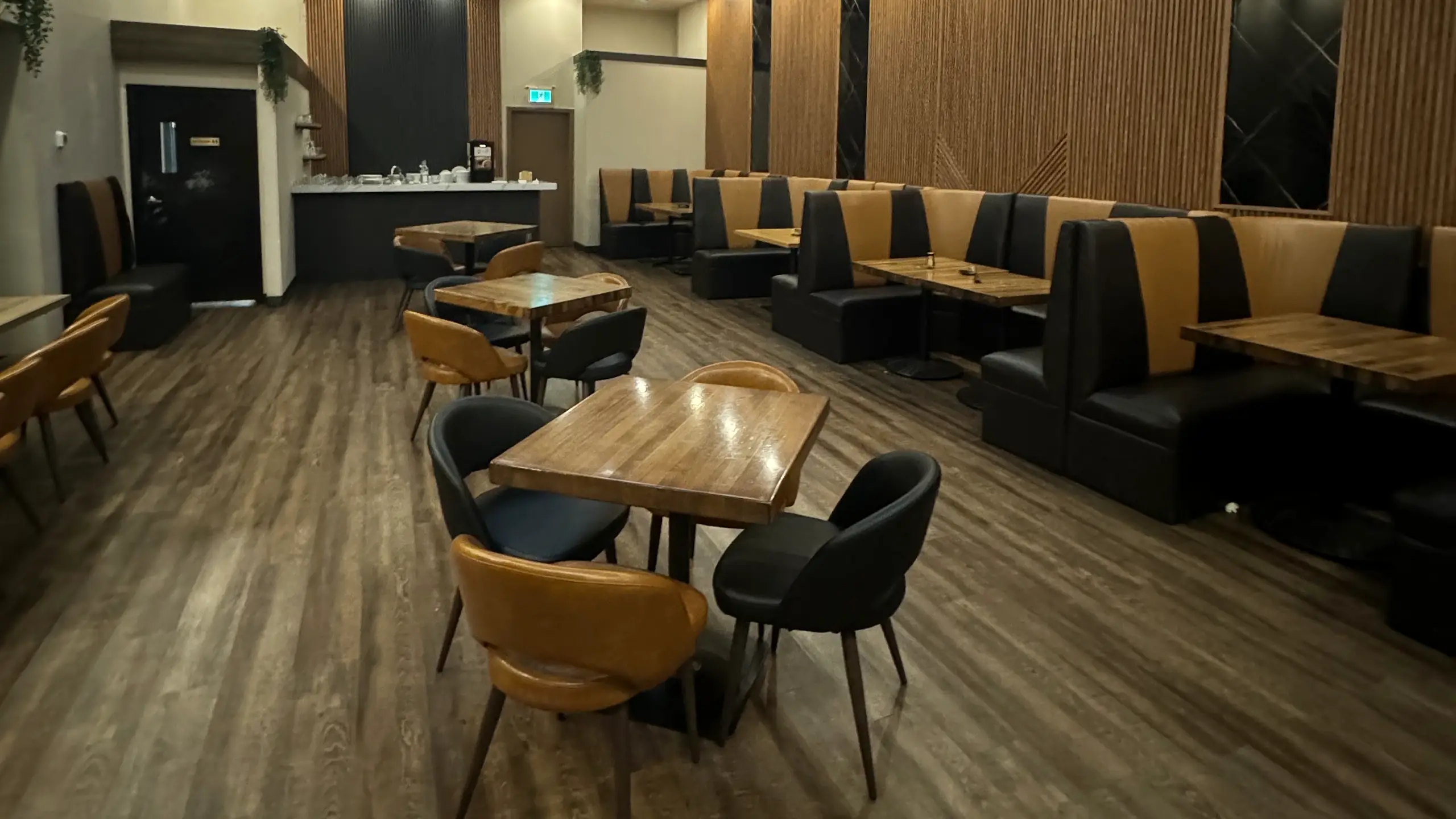 Dining room with wooden tables, black and tan chairs, booth seating and lit patterned ceiling panels