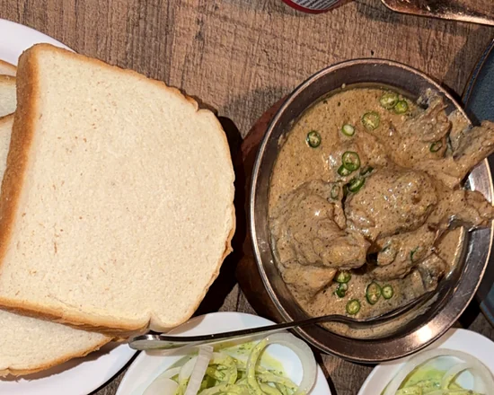Cream chicken in a pale creamy gravy with green chillies beside white bread slices