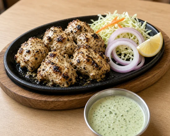 Black-pepper chicken tikka on a sizzler with onion rings, lemon and mint yogurt chutney
